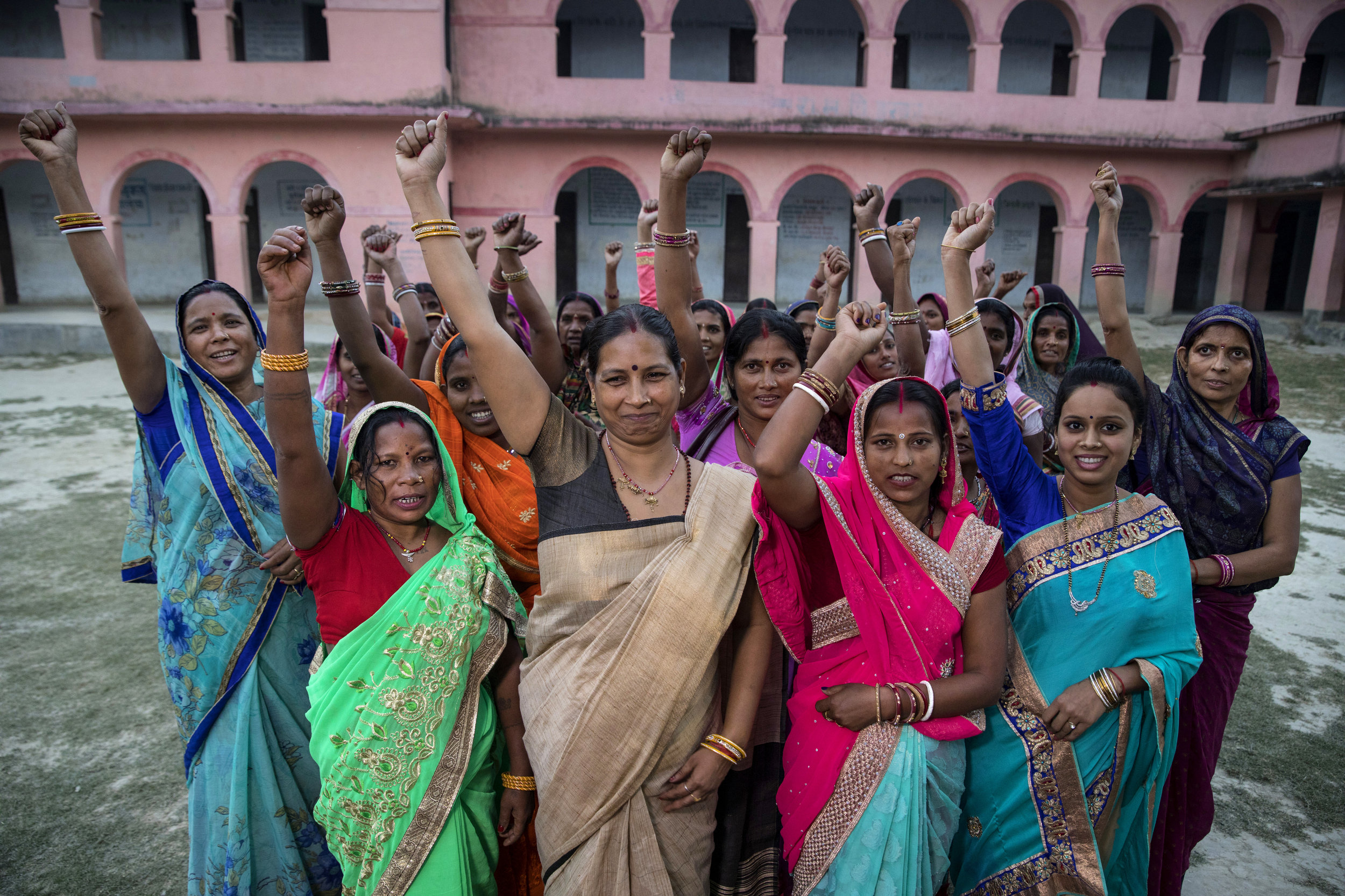 Empowered women wearing saris with arms upraised.