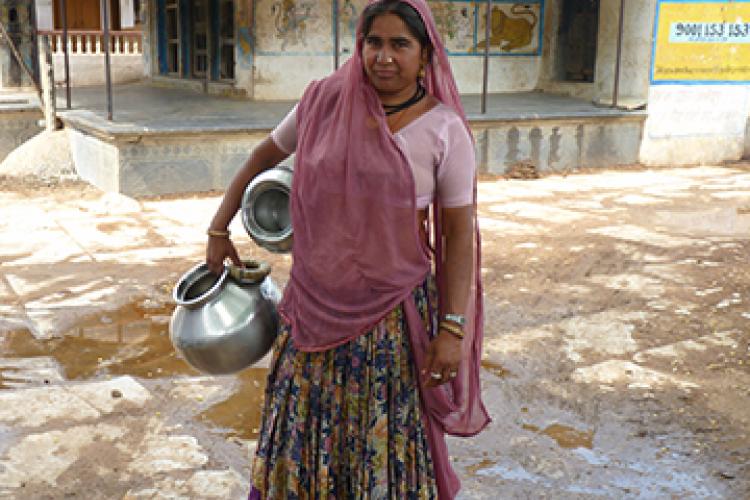 Indian woman in a sari stands with pots for gathering water