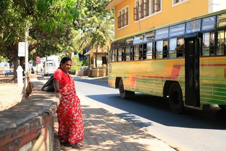 Woman in red sari waiting near yellow bus in India